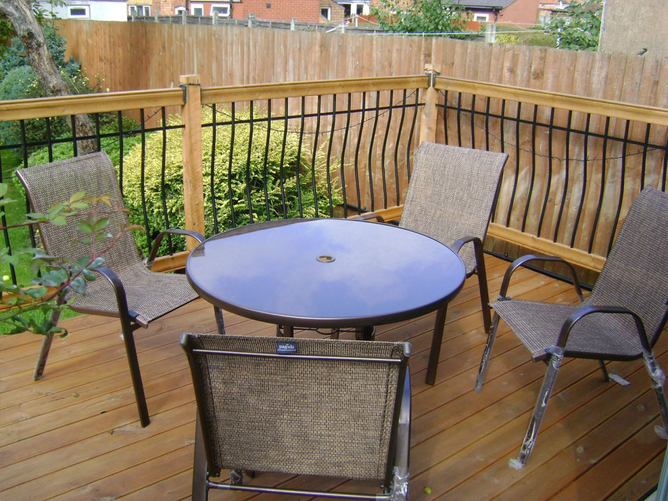 A photo of a table with 4 chairs around it, placed in a garden on top of wooden decking