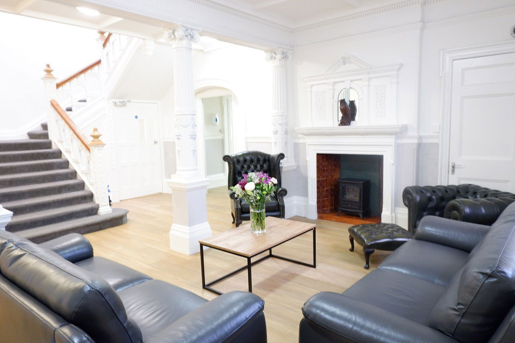A photo of Broadway Lodge communal seating area - with some sofas arranged around a glass coffee table placed in front of a fire place and a staircase