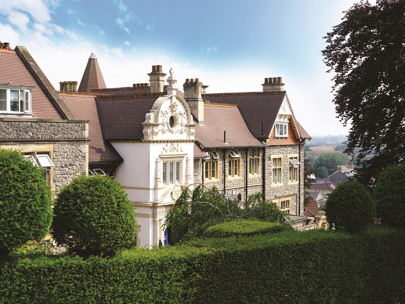The exterior of Broadway Lodge, with a garden and some bushes and trees in front