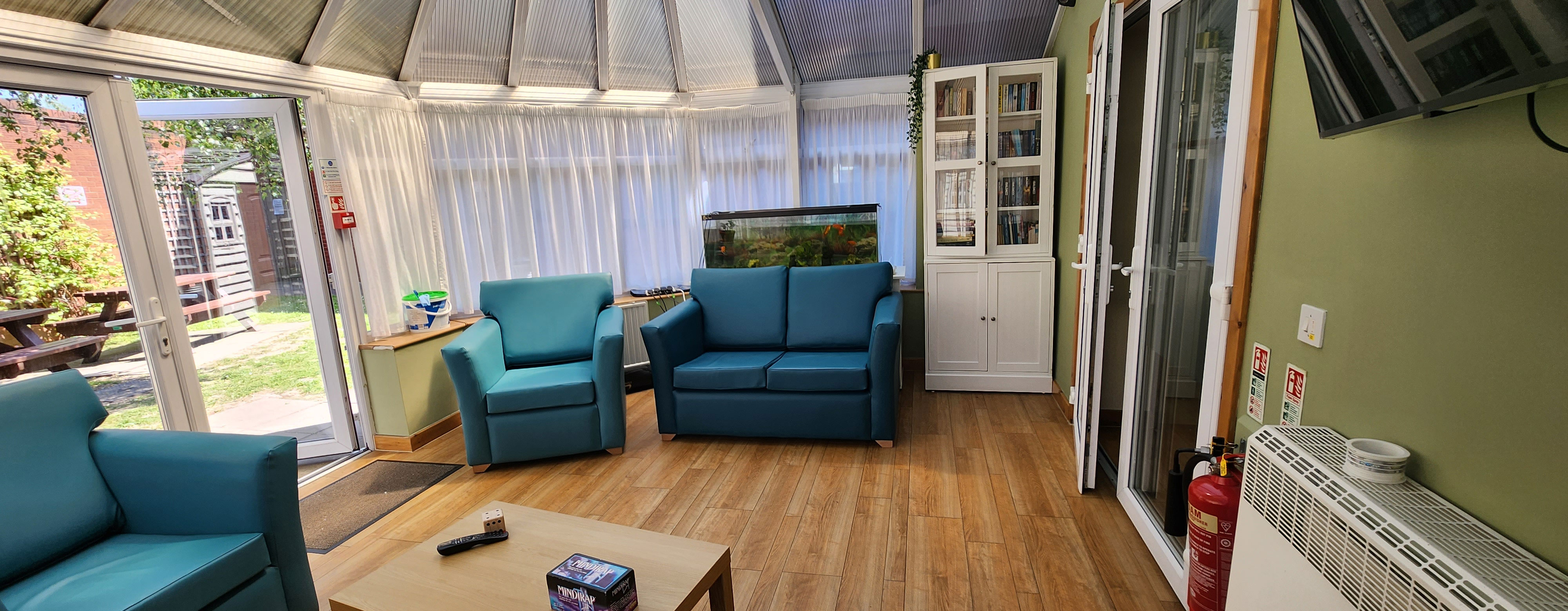 A conservatory. There is wooden floors and lots of windows letting in light. there are three arm chairs around the edge of the room.
