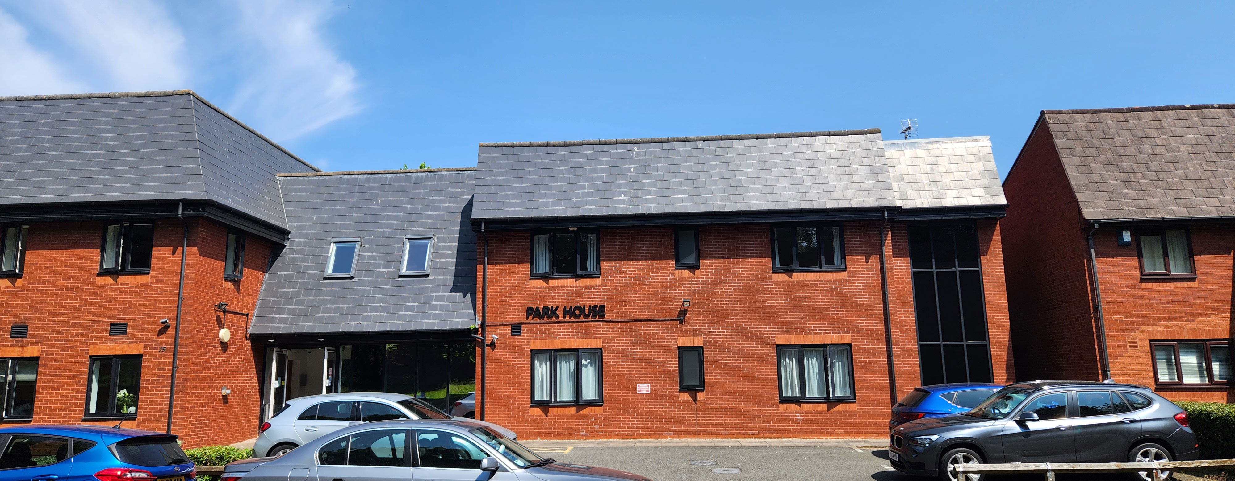 The outside of a modern building. It has red brick walls and a grey slate rood. There are cars parked outside and the words Park House and on the wall of the building