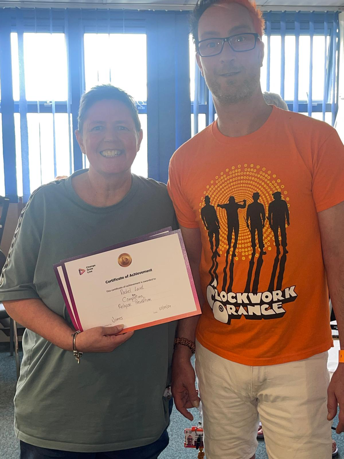 Two people stood smiling at the camera, one of them is holding up a certificate