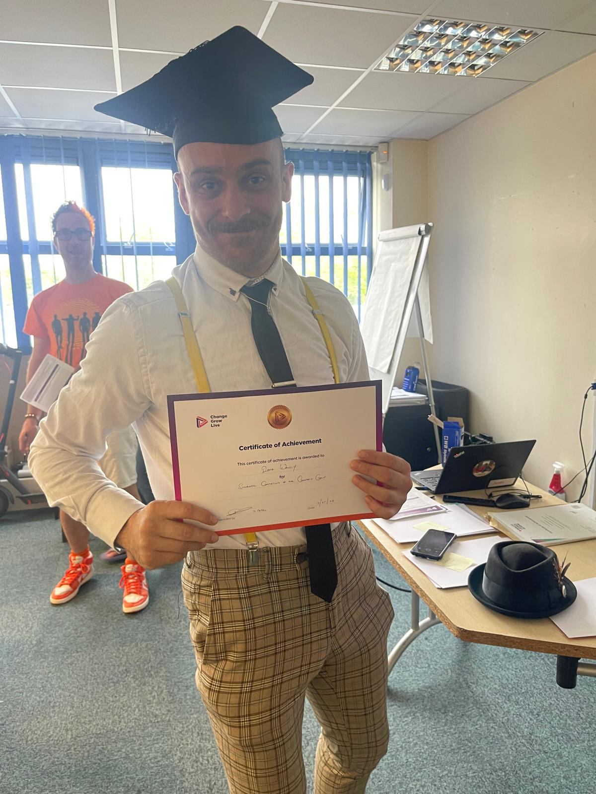 A man stood holding a certificate and wearing a graduation cap