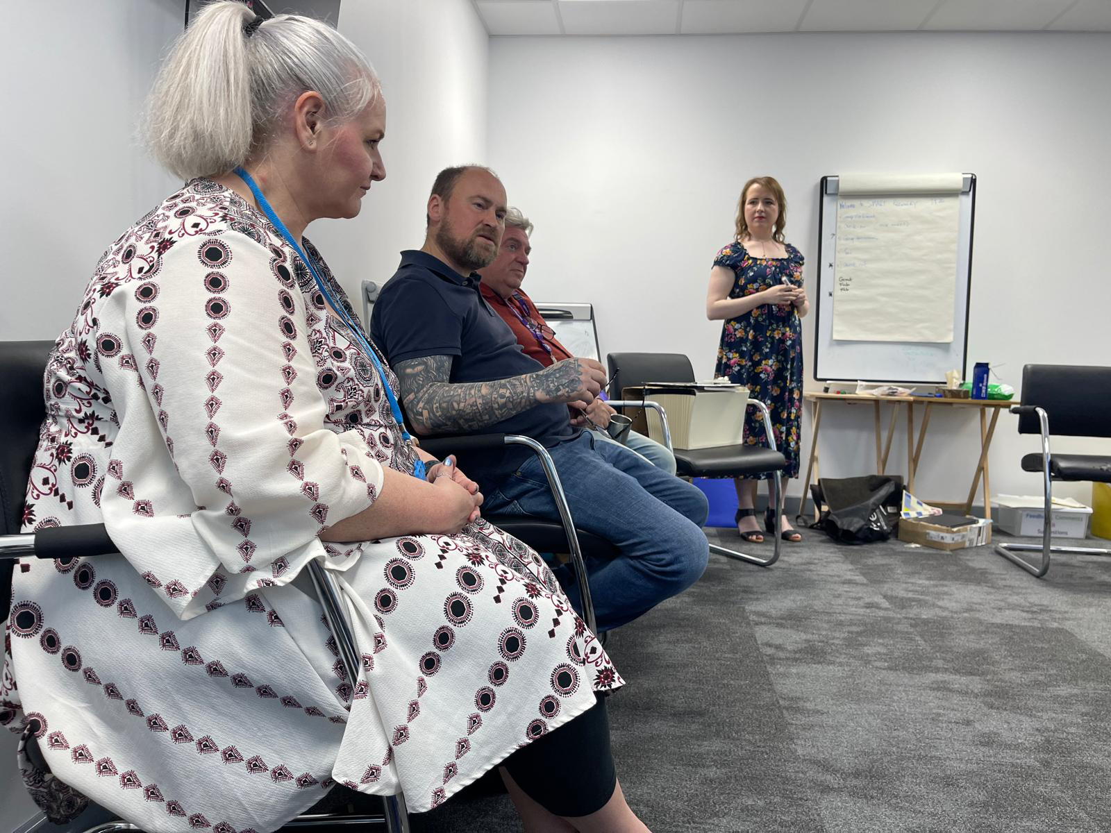 People sat in chairs around the edge of the room with a speaker stood in front of them