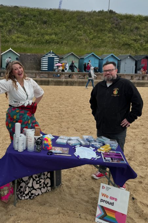 Two people stood on the beach with a table in front of them