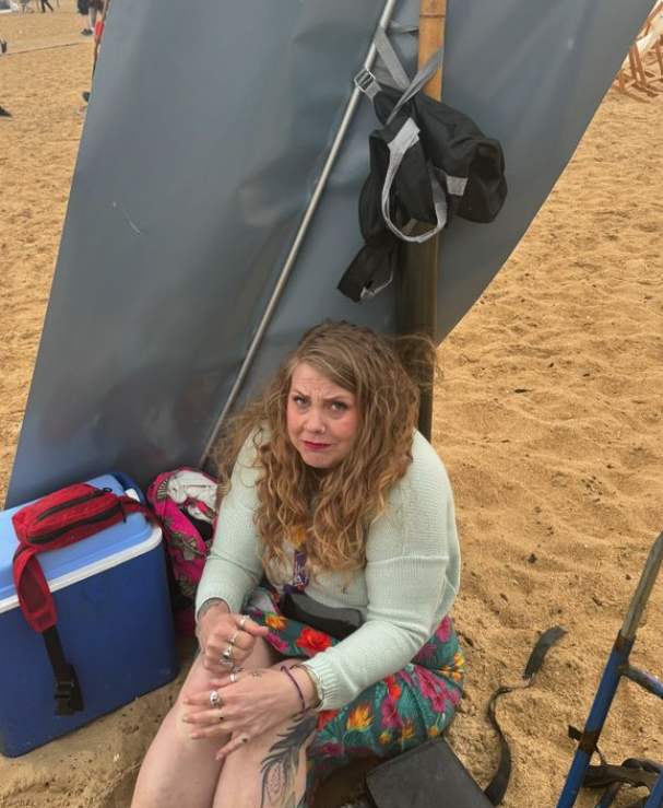 A young woman sand on the beach looking cold.