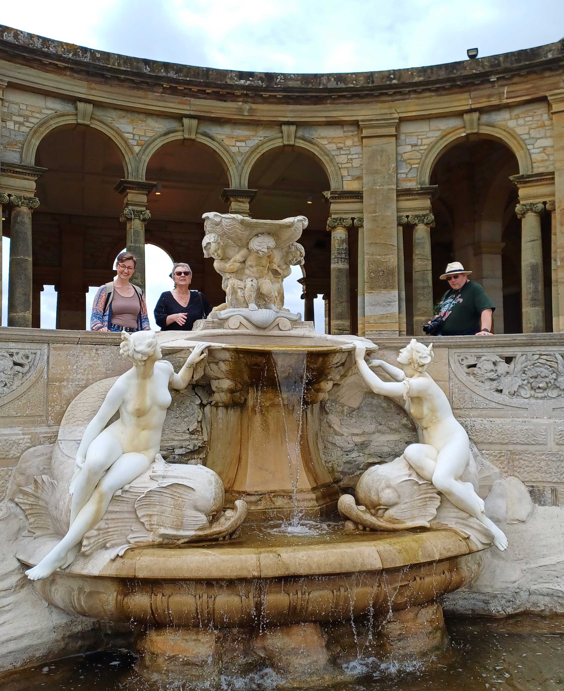 A water fountain with sculptures either side and archways behind