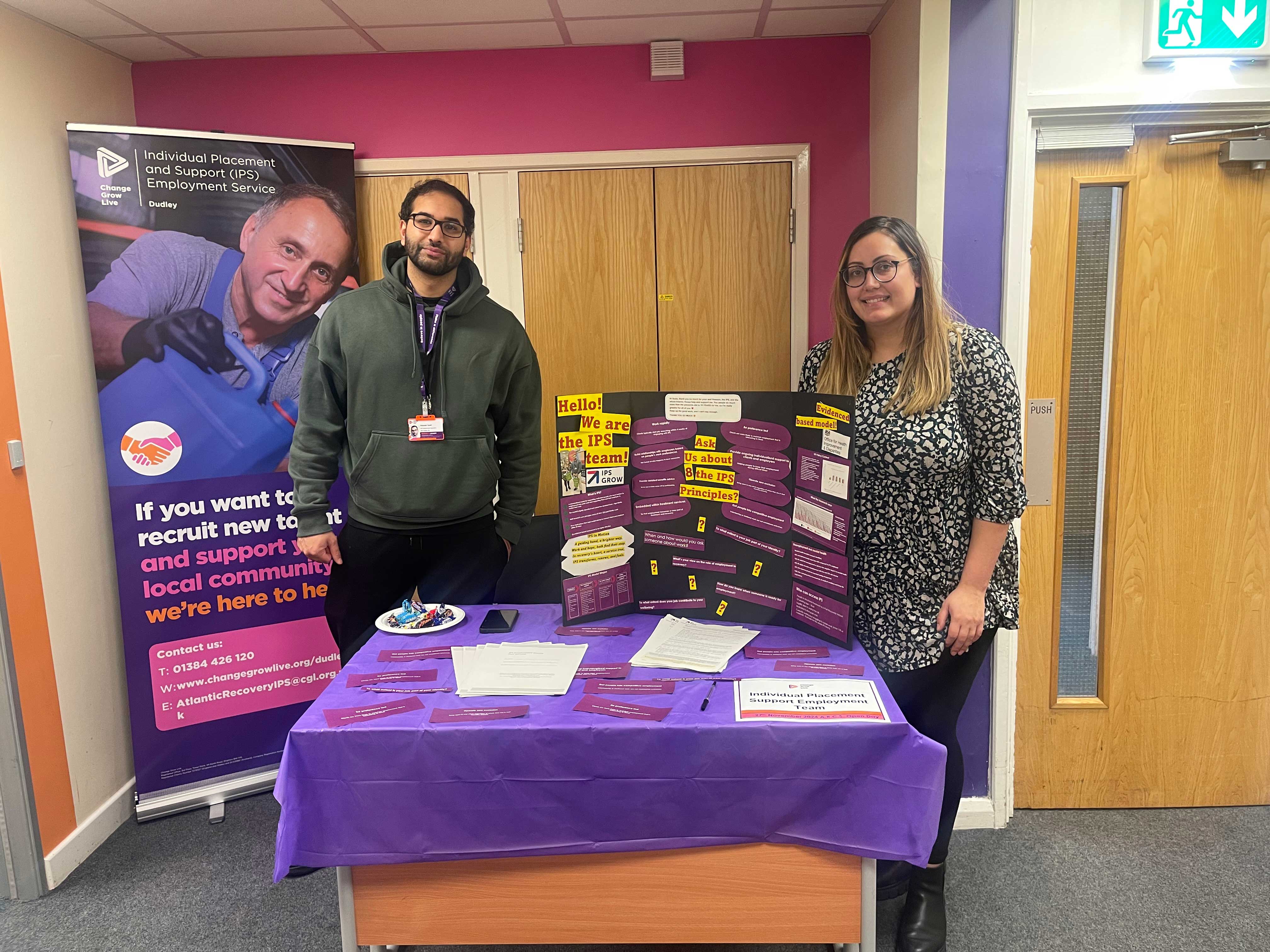 Two people stood behind a table with a purple tablecloth on it.