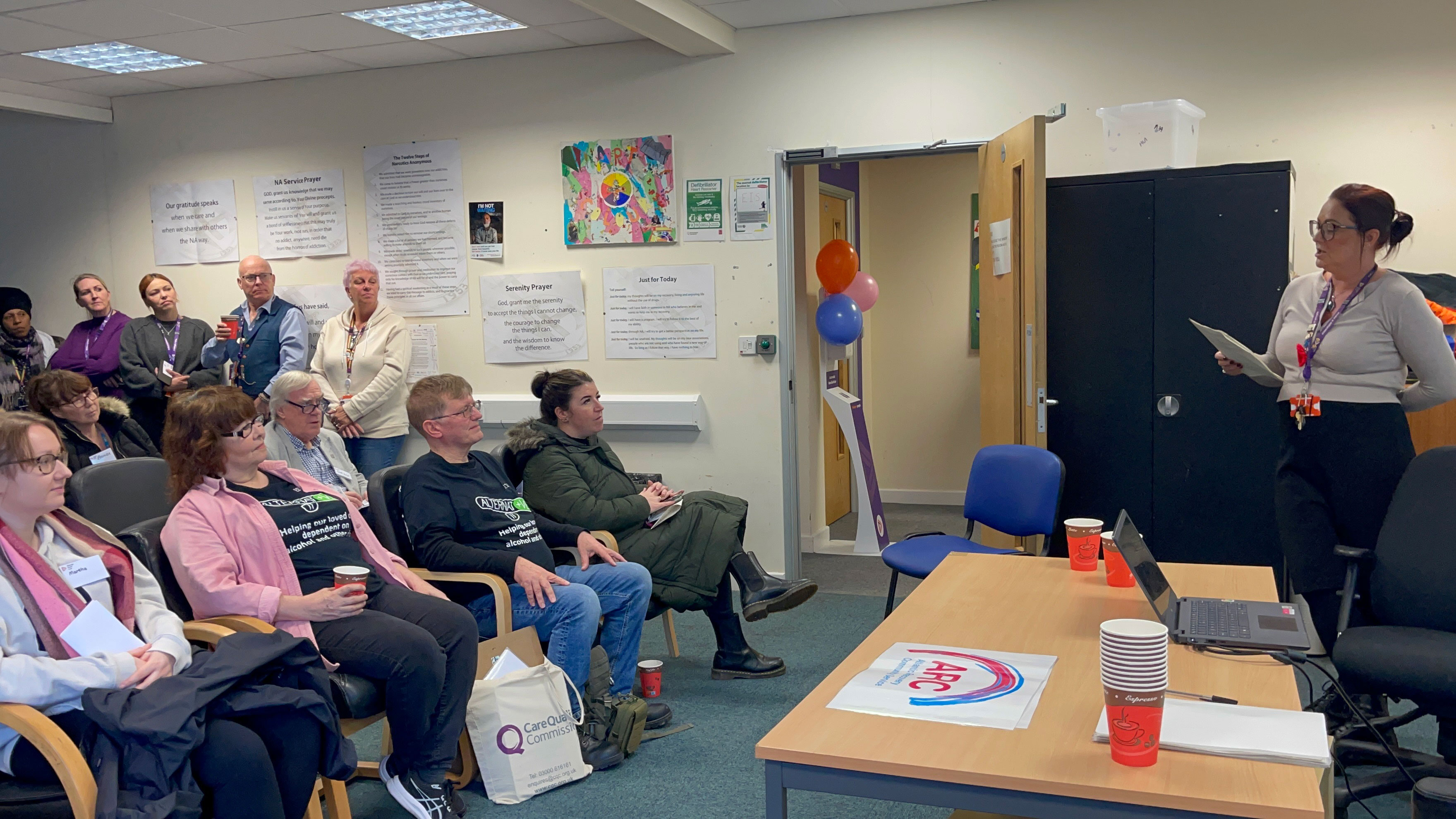 A woman giving a talk to an audience sat in chairs watching her.
