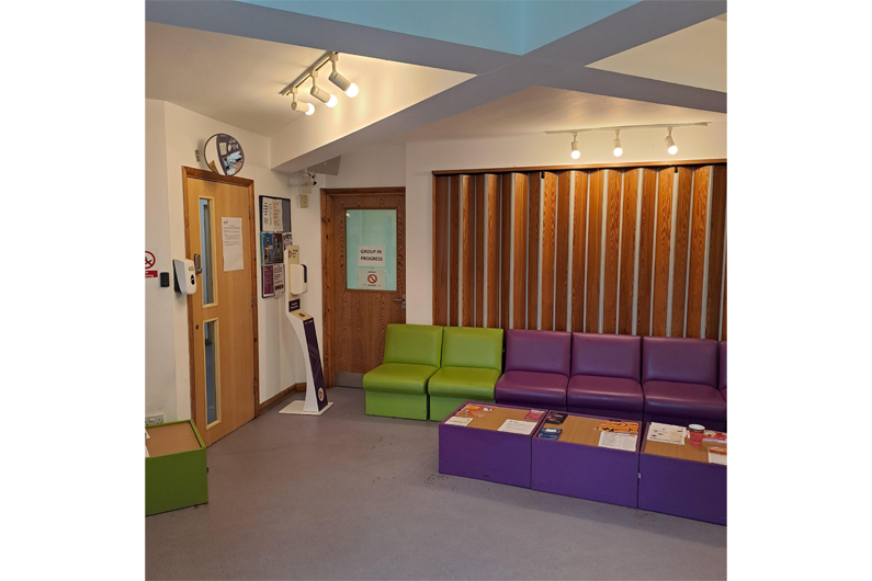An open room with wooden panelling on one wall and purple sofas in front of it