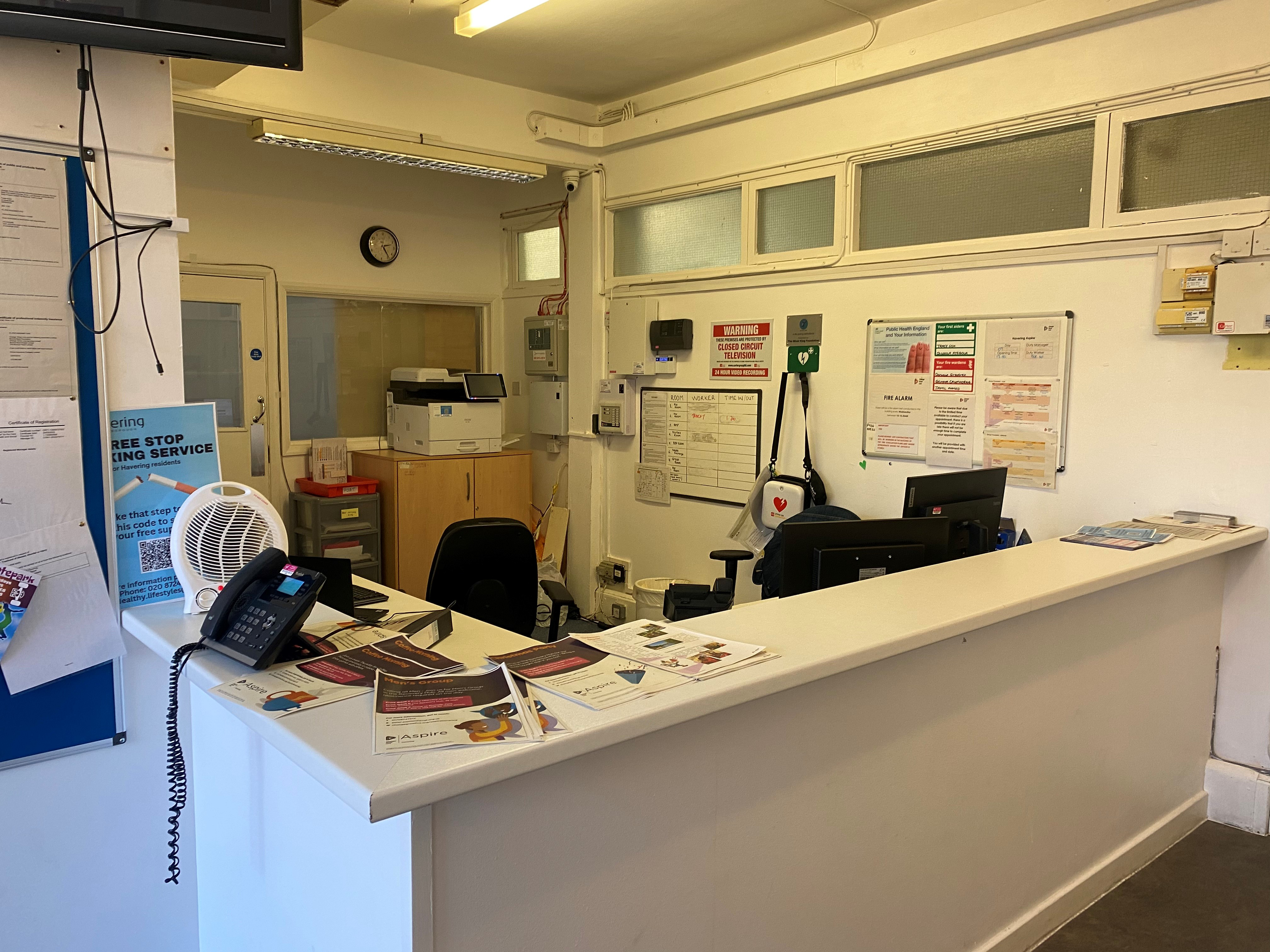 A reception desk with posters and leaflets, a fan, and chairs