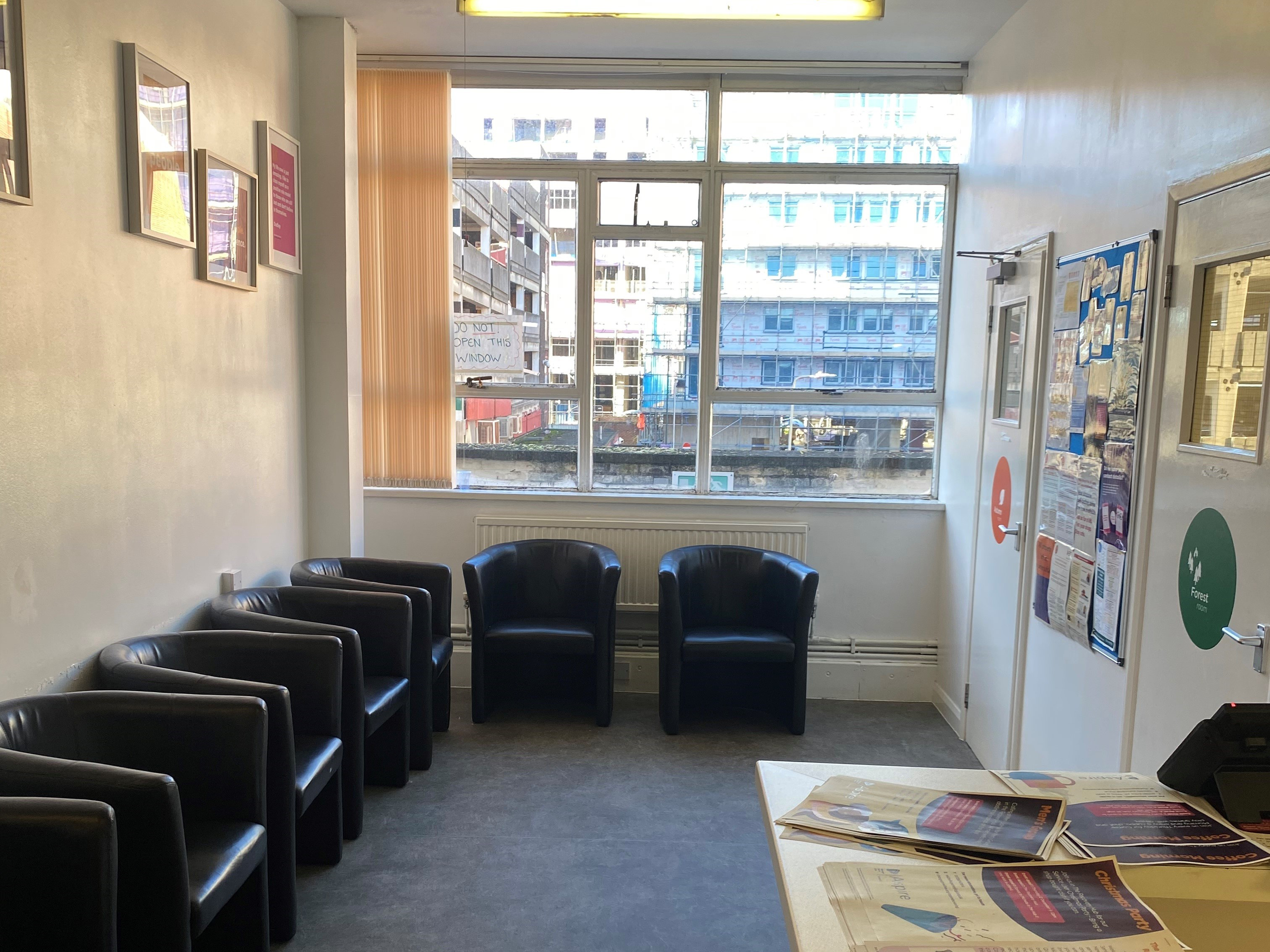 A waiting area with comfy chairs around the edge of the room. There are posters on the wall and a big window
