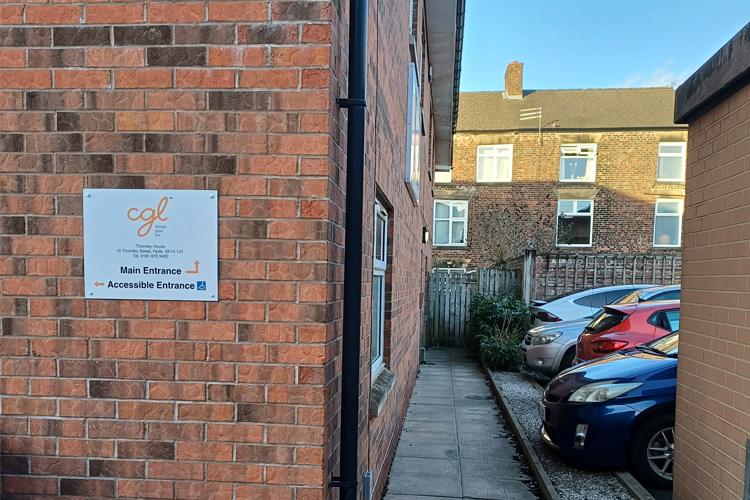 The corner of a brick building with a carpark next to it.