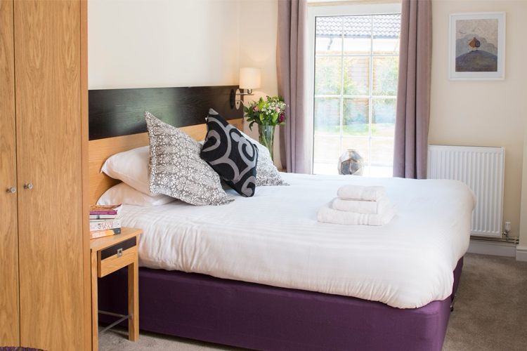 A spacious double bed with bed side table, wardrobe and large window looking out into the garden