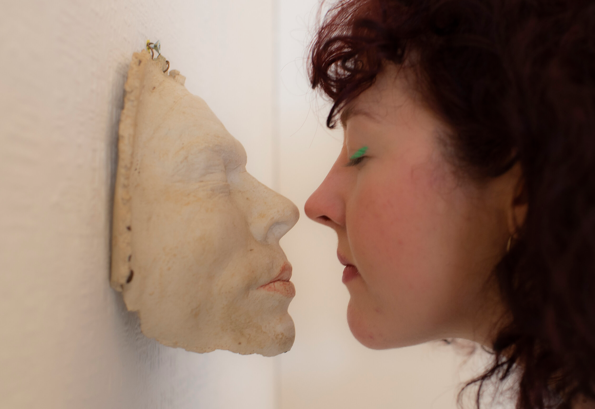 A woman putting her face against a sculpture of a face.