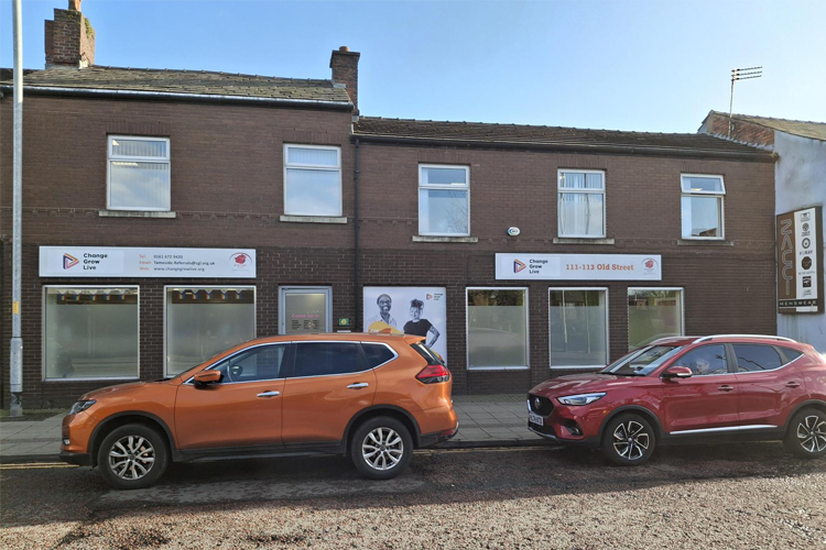 The outside of a brick building with signs above the door of Change Grow Live and cars parked on the street infront