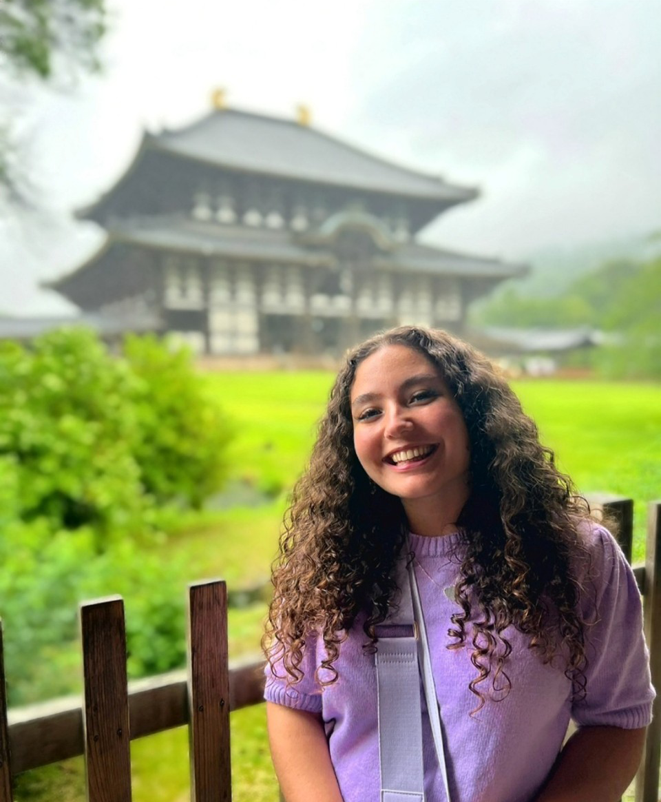 A young woman with long curly hair wearing a purple jumper