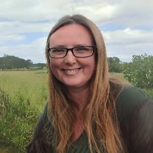 Donna has long blonde hair and wears glasses, she is out in the countryside.