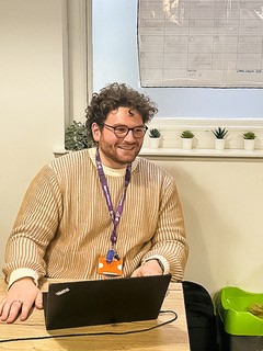 photo of an adult male smiling sat at a desk with a laptop