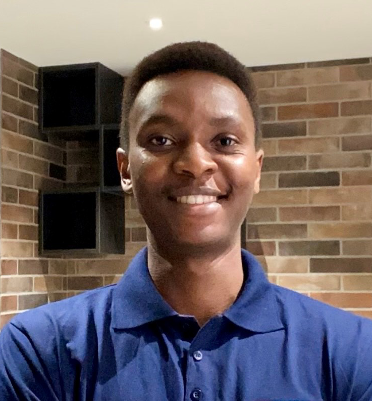 A young black boy wearing a navy blue polo neck shirt and smiling at the camera.