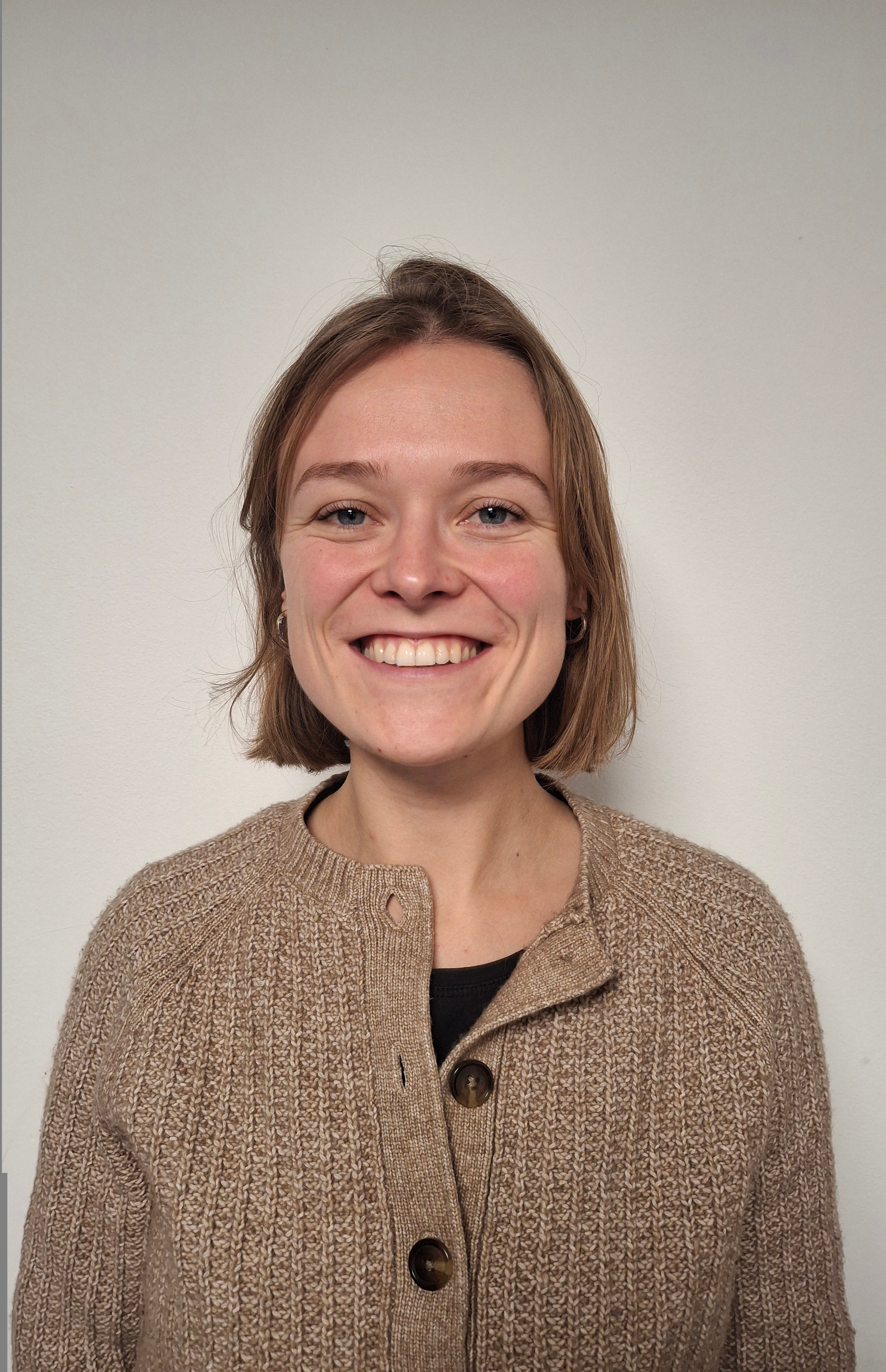 A young woman with a blonde bob wearing a brown cardigan