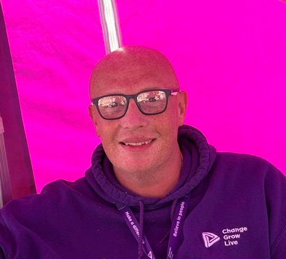 A bald man wearing glasses and a purple hoody sat inside a pink tent