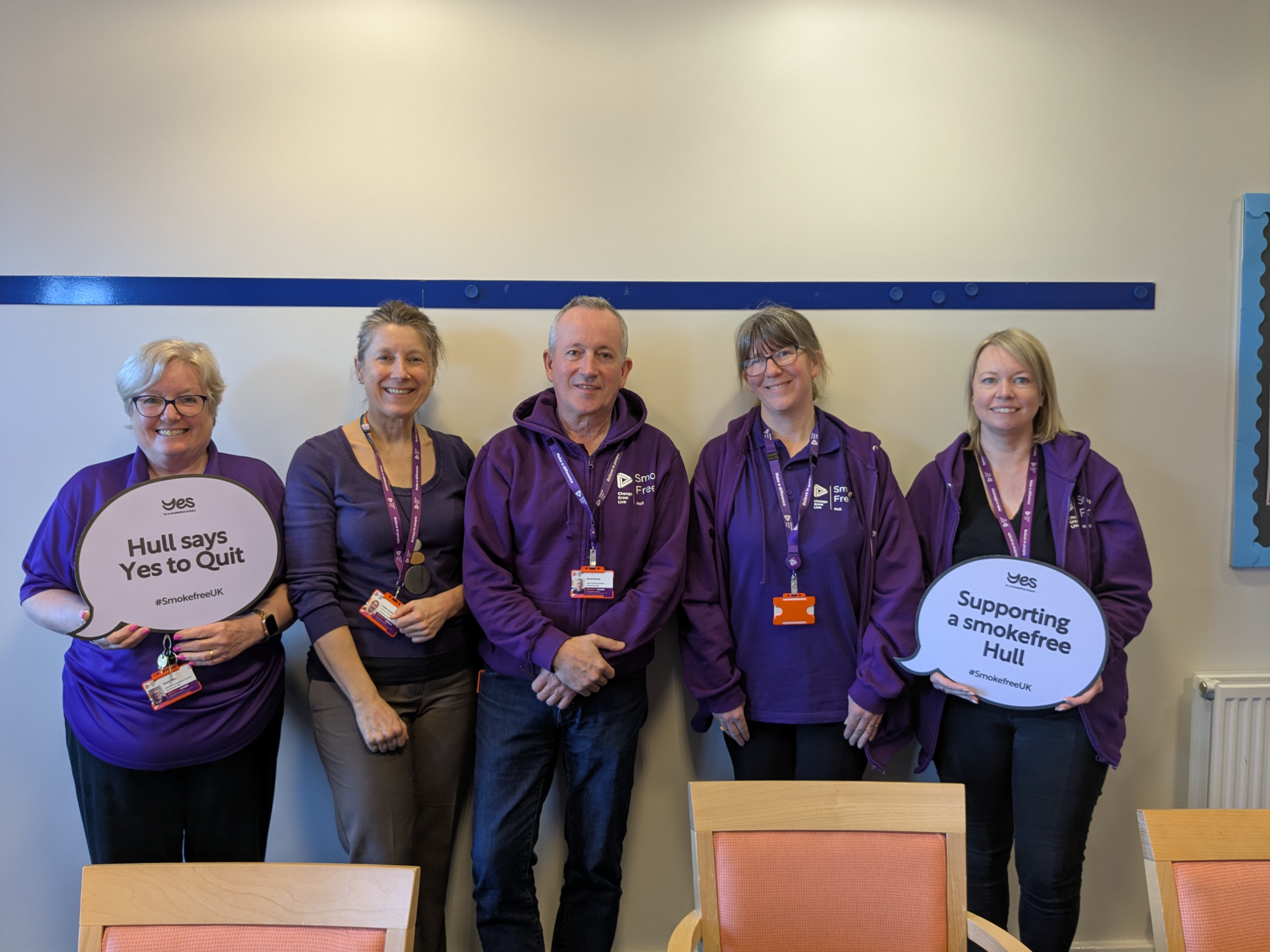 Five people stood in front of a wall wearing purple t-shirts