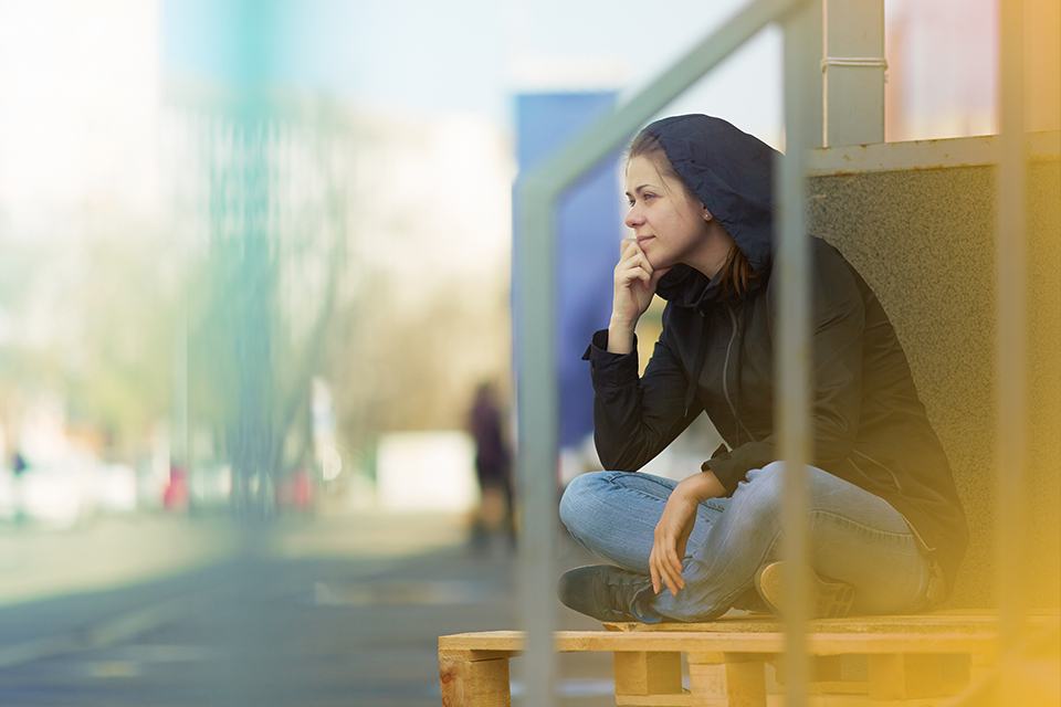 A stock photo of a young woman sitting outside staring into the middle distance