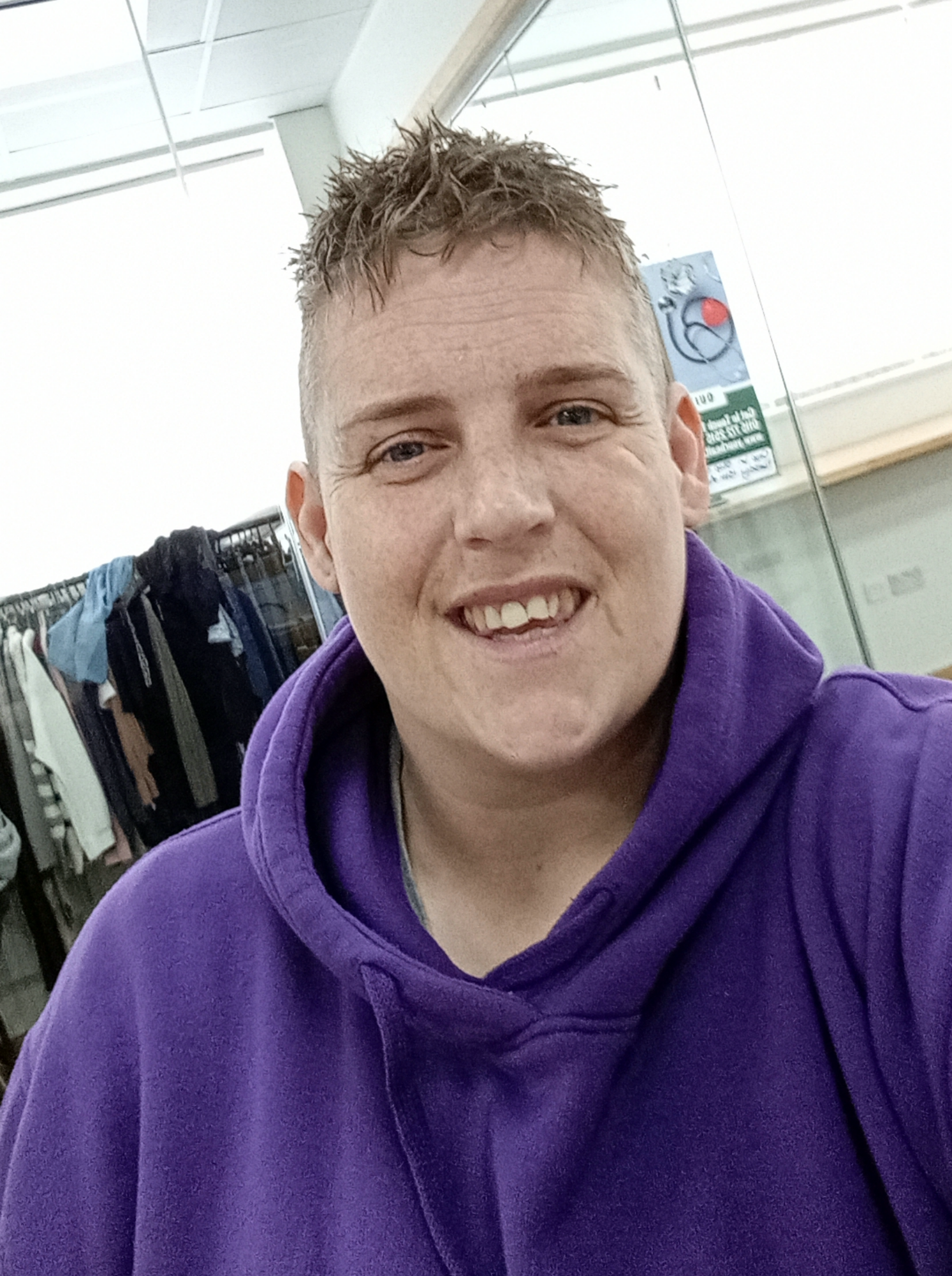 A woman with short, back and sides hair cut, smiling at the camera wearing a purple hoodie
