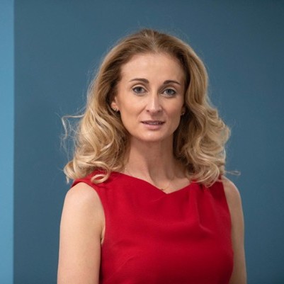 Victoria, our Trustee, wearing a red dress and with shoulder length hair, looking at the camera