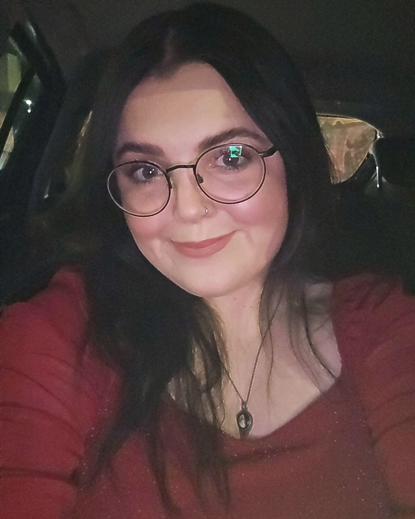 Katy has long brown hair and is wearing a red long sleeve top and round glasses.