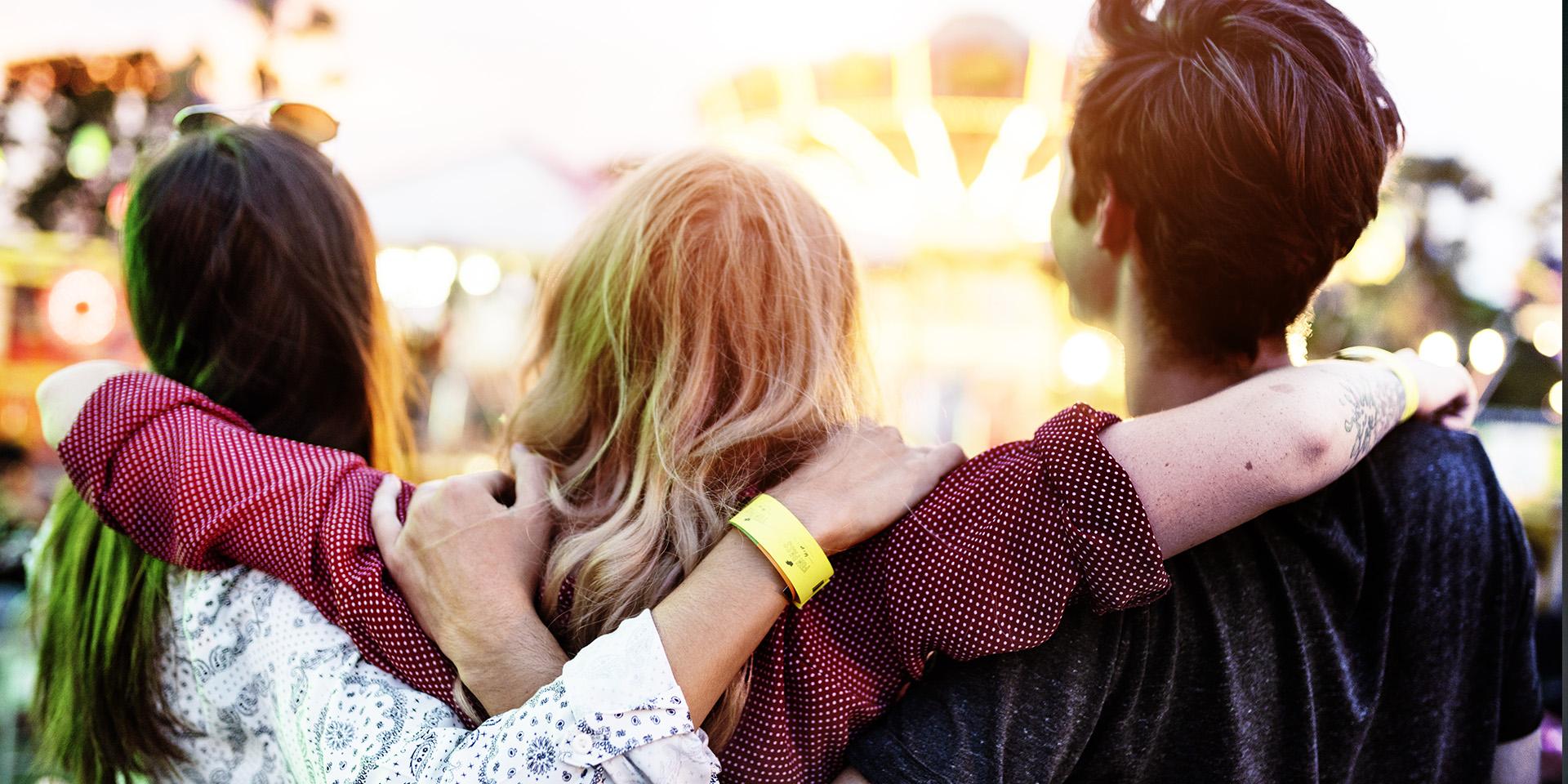 Trio of young people with their backs to the camera and their arms around each other 