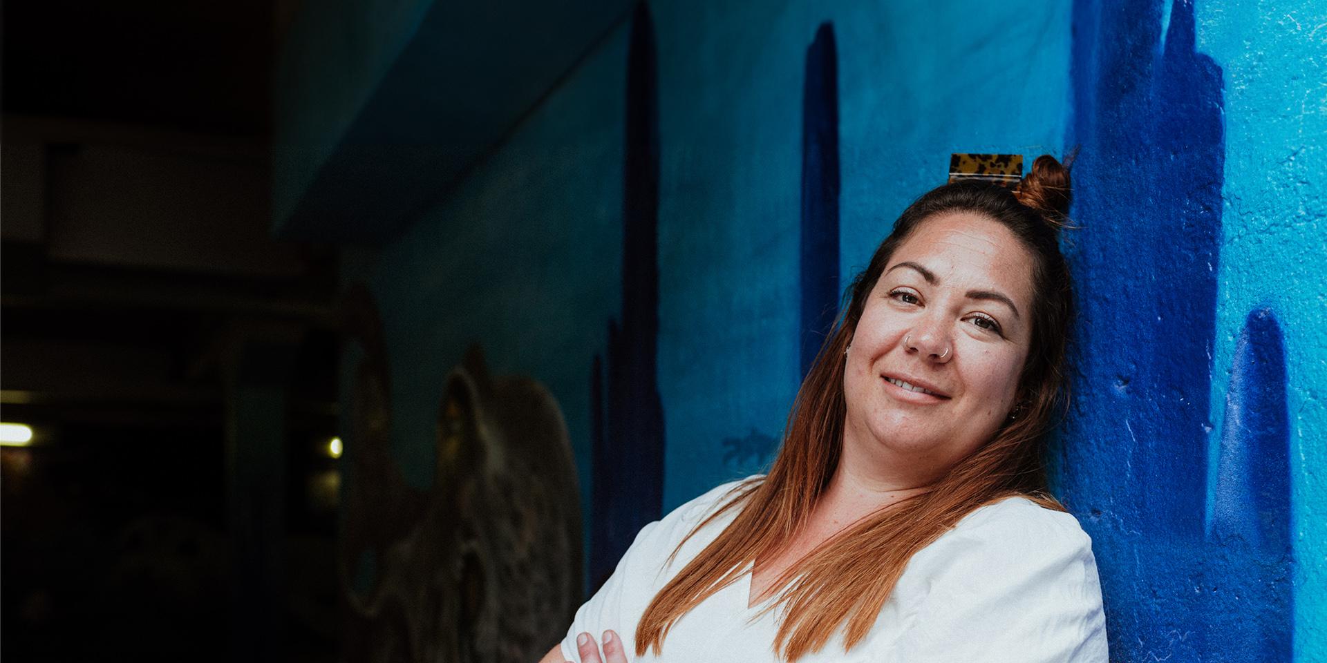 A person slightly smiling at the camera with a blue mural background