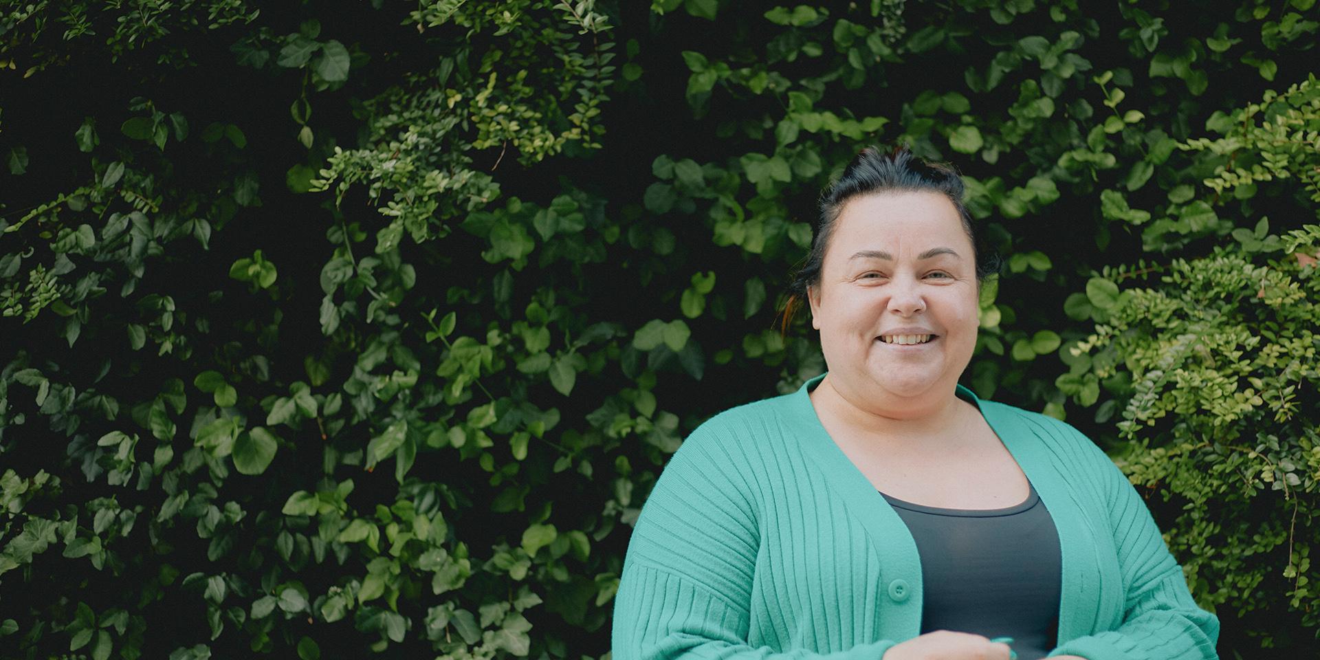 A smiling person looking at the camera with foliage in the background