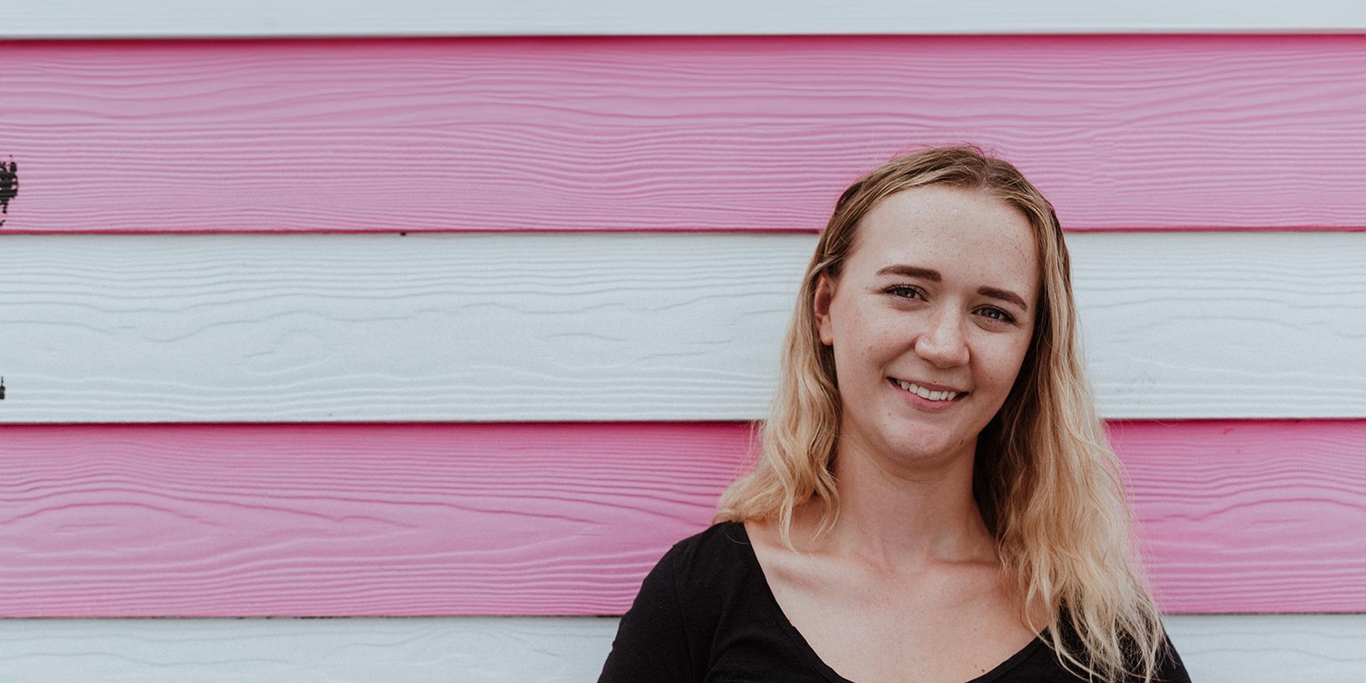 A person smiling against a pink stripe background 