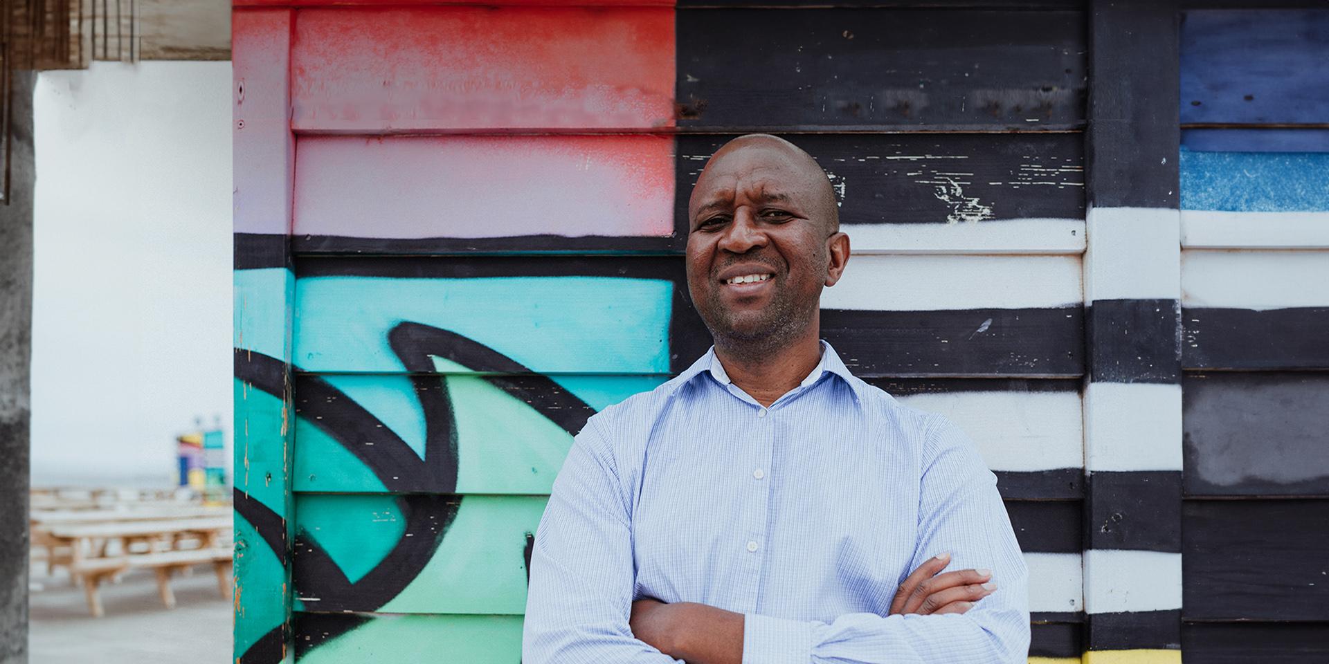 A person smiling at the camera with a mural in the background