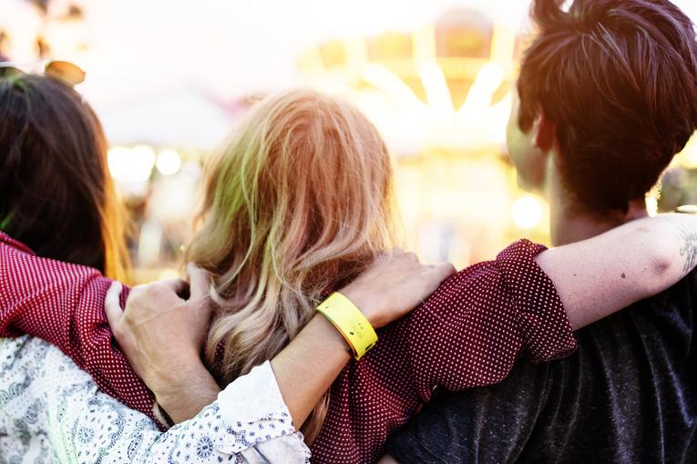 Trio of young people with their backs to the camera and their arms around each other 