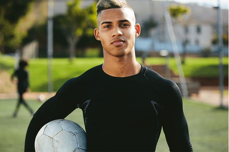 a young man holding a football under his arm looking directly to camera
