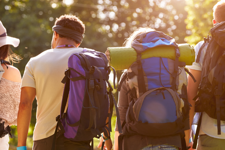 A group of people walking forward with backpacks on facing away from the camera