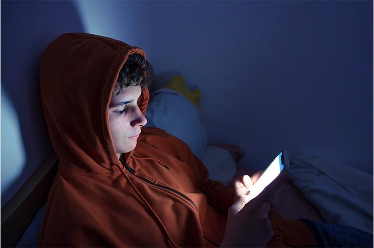 A teenager laying in bed scrolling his phone at night