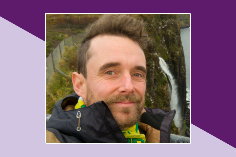 Joe is smiling at the camera, is photo is set on a background of dark and light purple