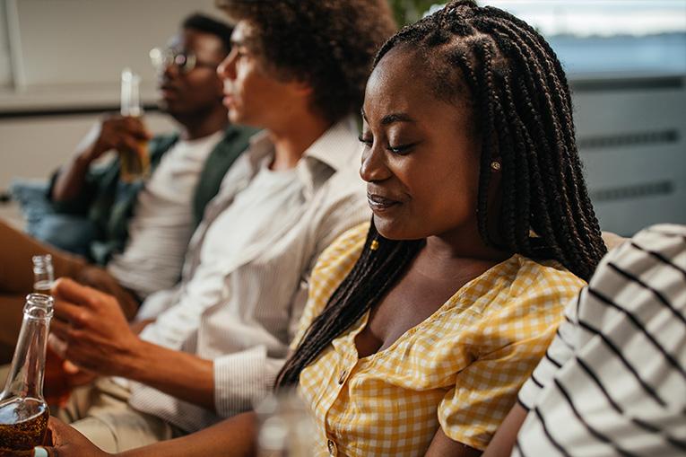 A young woman at a party holding a beer while looking pensive
