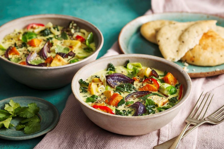 Two bowls of vegetable curry and a plate of naan bread