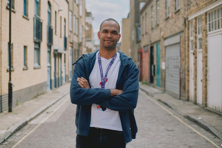 Luis stands in a cobbled street, arms folded with a gentle smile