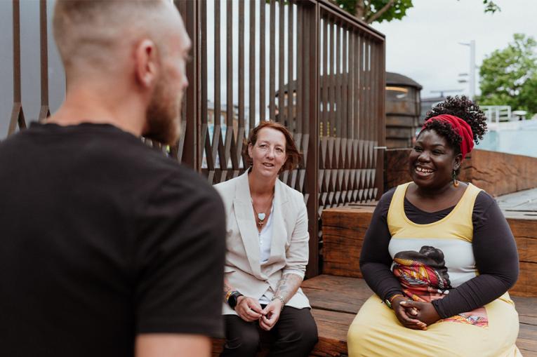 Three people talking to each other, one with their back to the camera