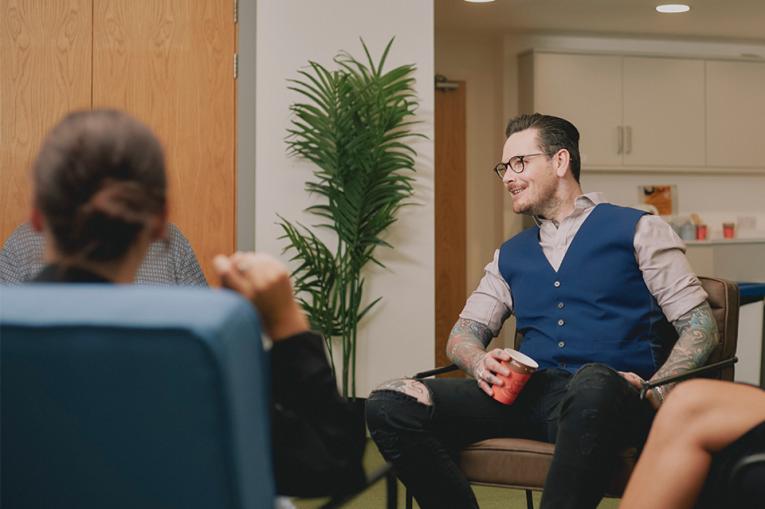 Neil sits in service relaxed drinking a coffee and chatting with colleagues