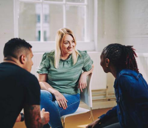 woman smiling sitting on a chair talking to two people