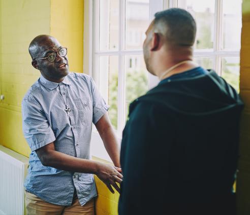 Dudley is standing against a bright yellow brick wall engaged in conversation