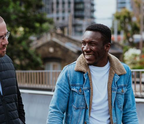 Two people walking outside near water, laughing and chatting