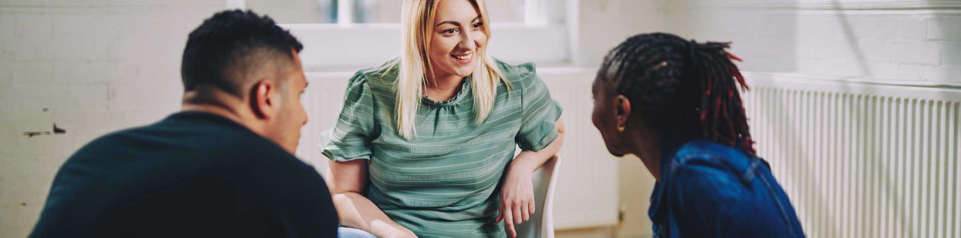 woman smiling sitting on a chair talking to two people